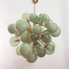 a green chandelier hanging from a gold colored ceiling fixture with glass globes