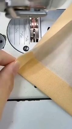 someone is sewing something on a machine with yellow tape around the edges and two hands