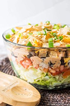 a salad in a glass bowl with dressing on top and a wooden spoon next to it