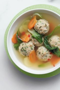 a white bowl filled with soup and meatballs on top of a green striped plate