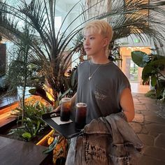 a young man carrying two drinks on a tray in front of plants and palm trees