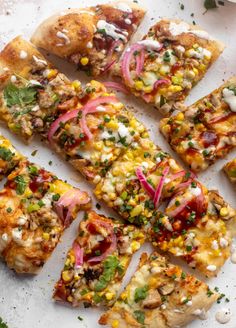 several slices of pizza with various toppings on a white surface next to some green leaves