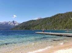 people are standing on a dock at the edge of a body of water with mountains in the background