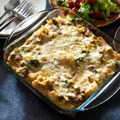 a casserole dish with broccoli, cheese and meat in it next to a salad