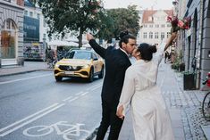 a newly married couple walking down the street with their arms in the air and holding hands