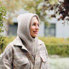 a woman wearing a hooded jacket standing next to a tree and shrubbery in the background