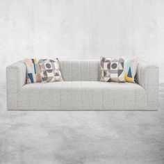 a couch with two pillows on top of it in front of a concrete wall and floor