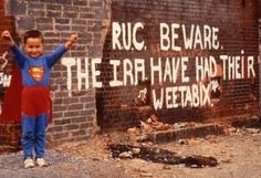 a young boy standing in front of a brick wall with graffiti on it and the words ruc beware, the urn have had their heart