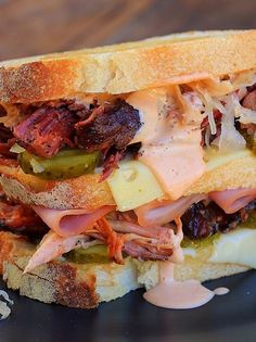 a sandwich with meat, cheese and pickles sitting on a black plate in front of a wooden table