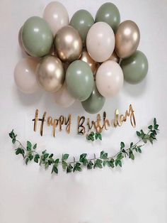 a bunch of balloons that say happy birthday and some greenery on the wall behind it