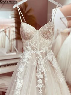 a white dress hanging on a rack in front of a piano and other wedding gowns