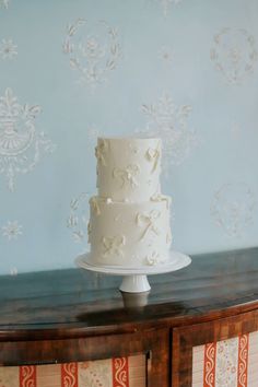 a white wedding cake sitting on top of a wooden table next to a blue wall