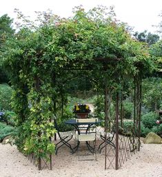 a table and chairs under an arbor in a garden