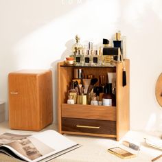 a wooden cabinet filled with lots of beauty products next to a mirror and magazine on the floor