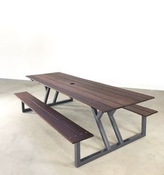 a picnic table with two benches in front of it on concrete floored area next to white wall