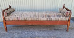 an old wooden daybed with two pillows on it's back and arms, sitting in front of a building