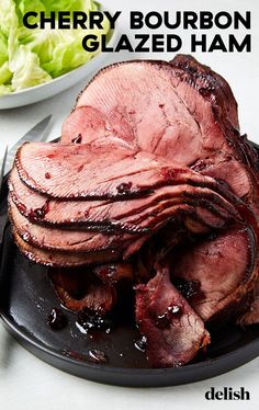 a plate with sliced meat on it next to a bowl of lettuce and a knife