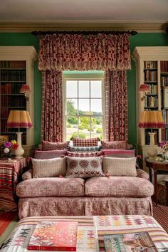 a living room filled with furniture and bookshelves next to a window covered in curtains