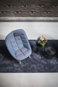 a blue chair sitting next to a small table with flowers on it and a brick wall in the background