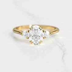 a three stone diamond ring on a marble surface with the center setting in yellow gold