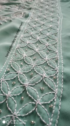 a close up view of the beading on a green fabric with white thread and beads