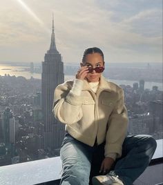 a woman sitting on top of a tall building talking on a cell phone while wearing sunglasses