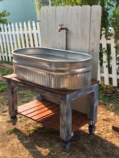 an old metal tub sitting on top of a wooden table next to a white picket fence