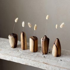 four wooden vases sitting on top of a table with white flowers in them and one has long grass sticking out of it