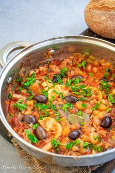 a large pot filled with lots of food on top of a table next to a loaf of bread