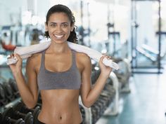 a woman in a gray sports bra holding up two white towels over her shoulders and smiling at the camera