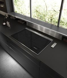 a kitchen counter with a stove top in front of a large window that looks out onto the woods