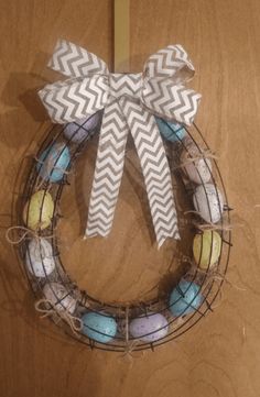 a wreath made out of colored eggs with a bow on the front and side hanging on a door