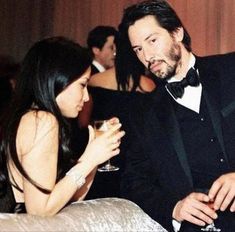 a man and woman sitting next to each other at a formal event with wine glasses in their hands