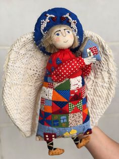 an angel doll with blue hat and red dress holding a book in her hand,