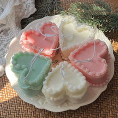 four heart shaped cookies sitting on top of a white plate next to pine branches and lace