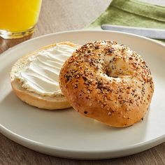 a bagel with cream cheese is on a plate next to a glass of orange juice