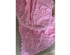 a pink knitted blanket sitting on top of a couch next to a basket filled with flowers