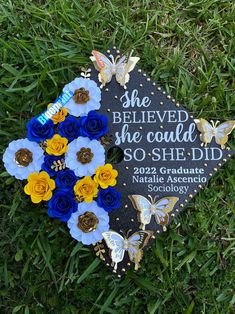 a blue and yellow graduation cap with flowers on it sitting in the middle of grass