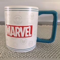 a white and blue coffee mug with the word marvel on it sitting on a carpet