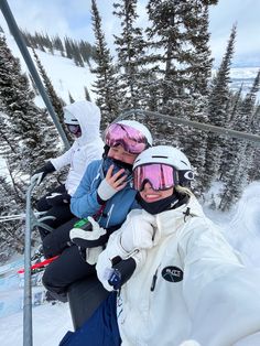 three people on a ski lift taking a selfie with their camera phone in the snow