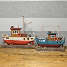 two small wooden boats sitting next to each other on top of a wooden table in front of a striped wall