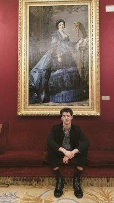 a man sitting in front of a painting on the wall next to a red couch