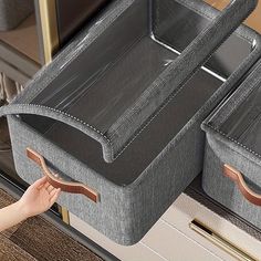 two gray storage bins with handles on each side and one holding a brown handle