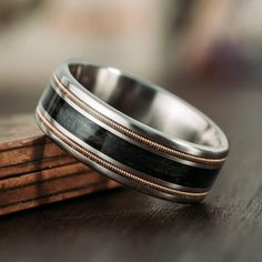 a wedding band with black and gold inlays sits on top of a piece of wood