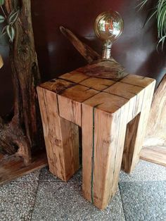 a small wooden table with a metal ball on it's top and some plants in the background