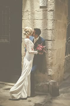 a bride and groom kissing in front of an old building with stone pillars on either side