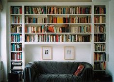 a black leather couch sitting in front of a book shelf filled with books on it