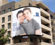 an advertisement on the side of a building for be one with two men hugging each other