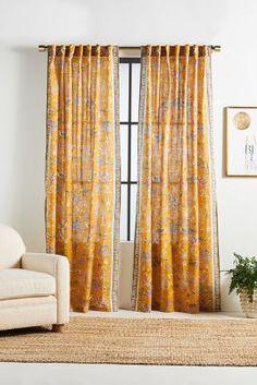 a living room with yellow curtains and a white chair in front of a window that has an orange flowered pattern on it