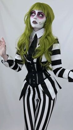 a woman with green hair and makeup is dressed in black and white striped clothing, holding her hands out